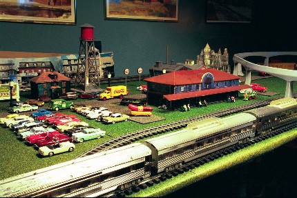 Model of the Lansdale Station, parking lot filled with cars and a commuter train going past.